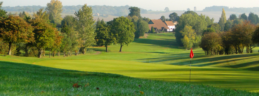 Archive view across Farthingstone’s green valley with mature trees, a red golf flag and the former hotel in the distance.